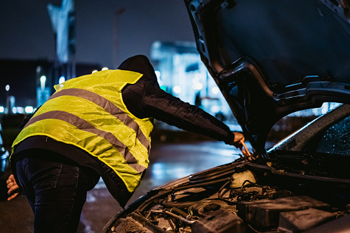 Man trying to repair car at sideroad at night.